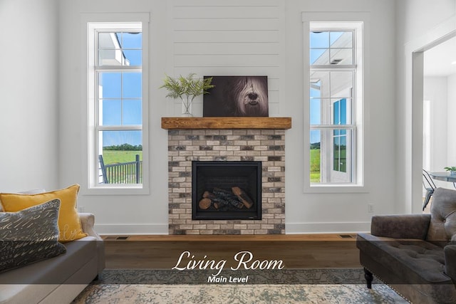 living room with a brick fireplace, baseboards, visible vents, and wood finished floors