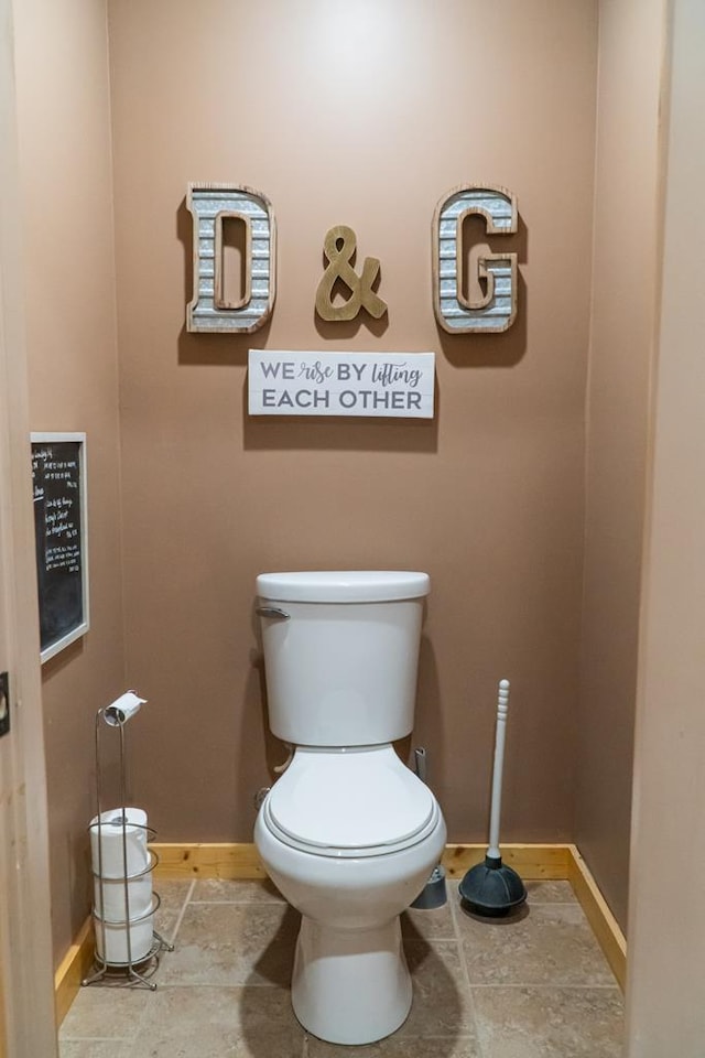 bathroom featuring stone finish floor, toilet, and baseboards