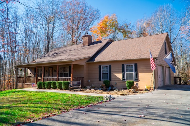 view of front of house with a garage, a chimney, aphalt driveway, covered porch, and a front yard