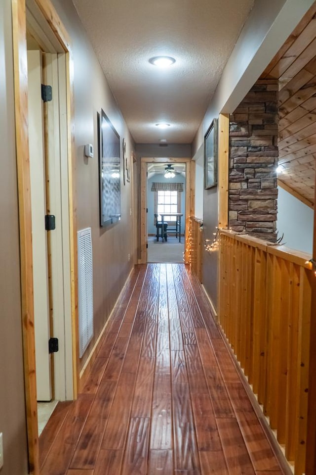 corridor with visible vents, dark wood finished floors, a textured ceiling, and baseboards