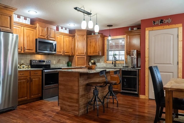 kitchen with wine cooler, a kitchen island, hanging light fixtures, light stone countertops, and stainless steel appliances