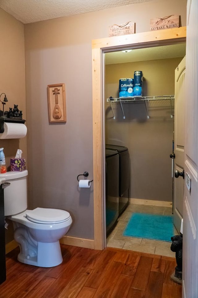 bathroom with washing machine and clothes dryer, toilet, a textured ceiling, wood finished floors, and baseboards