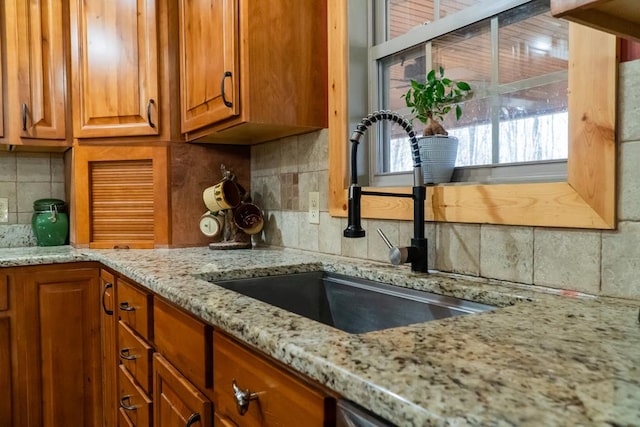 kitchen featuring tasteful backsplash, light stone counters, a sink, and brown cabinets