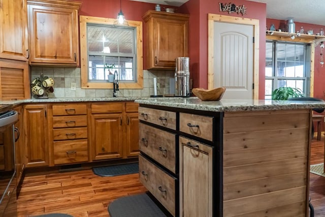 kitchen featuring stove, light wood-style floors, hanging light fixtures, light stone countertops, and brown cabinetry