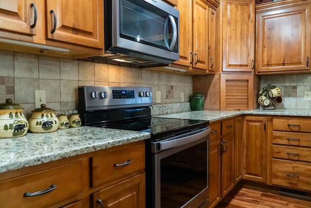 kitchen with light stone counters, brown cabinets, stainless steel appliances, decorative backsplash, and light wood-style floors