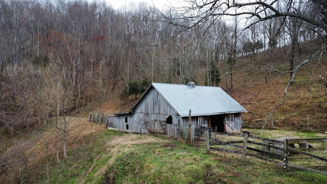 view of barn featuring fence and a wooded view