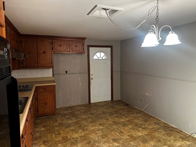 kitchen featuring decorative light fixtures, light countertops, black cooktop, brown cabinetry, and under cabinet range hood