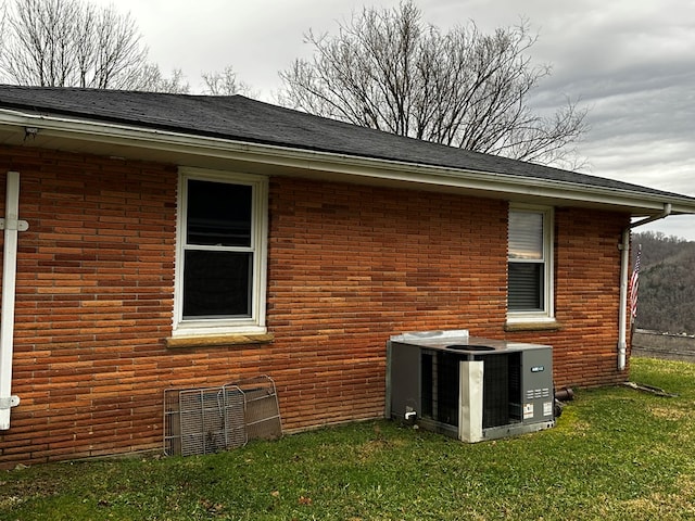 view of side of home with central AC, a lawn, brick siding, and roof with shingles