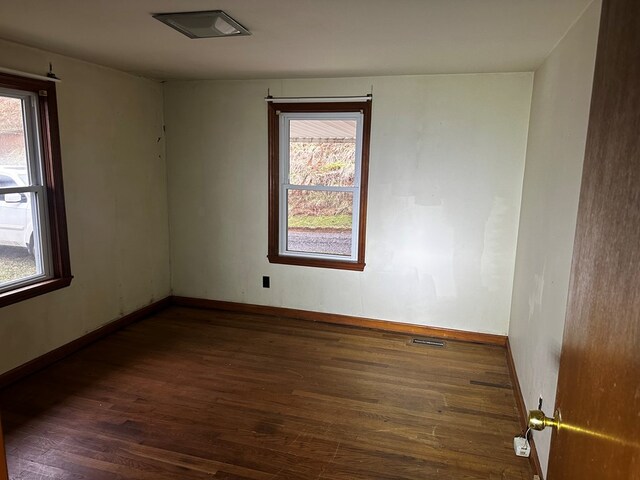 unfurnished room featuring dark wood-style floors, visible vents, and baseboards