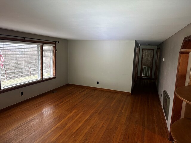 empty room featuring dark wood-style flooring, visible vents, and baseboards