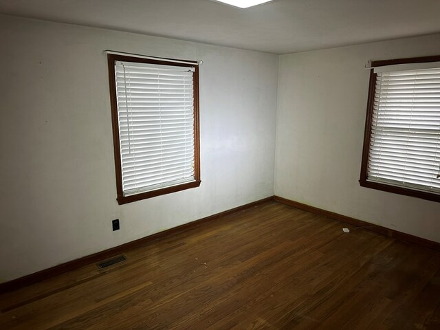 unfurnished room featuring baseboards, visible vents, and dark wood-style flooring