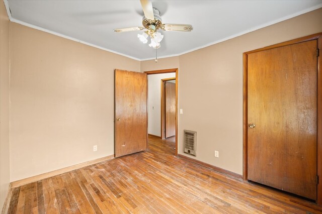 unfurnished bedroom with heating unit, wood-type flooring, ornamental molding, a ceiling fan, and baseboards