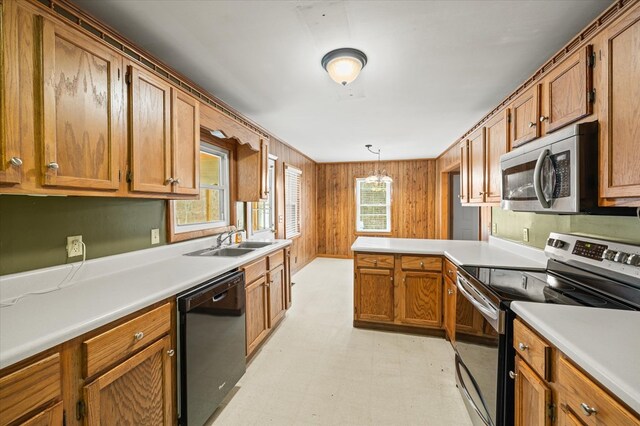 kitchen featuring wooden walls, a peninsula, a sink, appliances with stainless steel finishes, and light floors