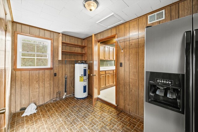 kitchen featuring wooden walls, water heater, visible vents, and stainless steel refrigerator with ice dispenser