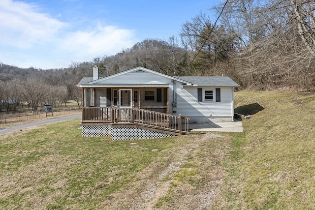 view of front of home with covered porch, a chimney, and a front yard