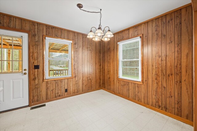 unfurnished dining area featuring visible vents, an inviting chandelier, wood walls, baseboards, and tile patterned floors