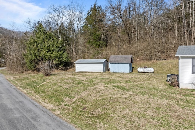 view of yard featuring a storage shed, a wooded view, central AC, and an outdoor structure