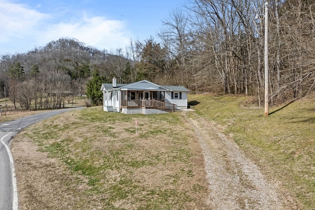 view of front of property featuring driveway, a porch, a view of trees, and a front yard