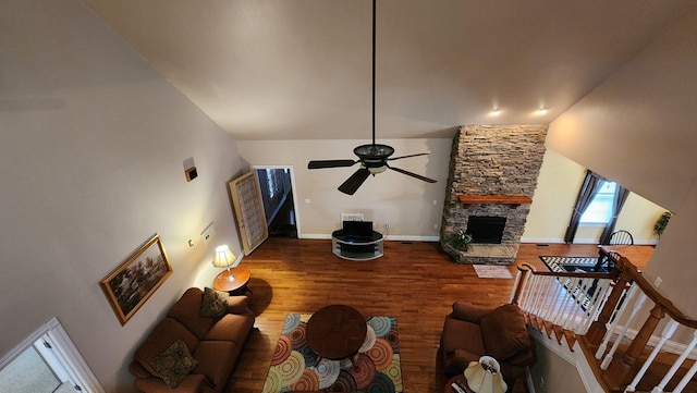 living area with ceiling fan, a stone fireplace, wood finished floors, and baseboards