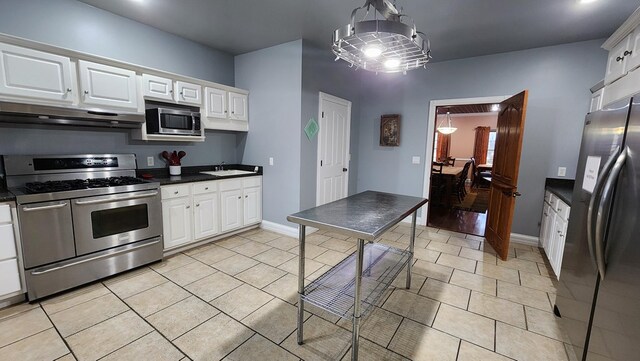 kitchen featuring stainless steel appliances, dark countertops, under cabinet range hood, and white cabinets