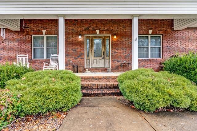 view of exterior entry featuring brick siding and a porch