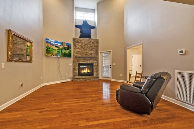 living room with visible vents, a stone fireplace, baseboards, and wood finished floors