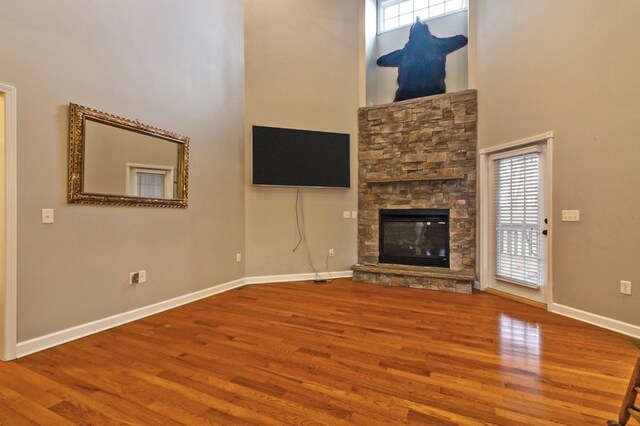 unfurnished living room with a wealth of natural light, a stone fireplace, baseboards, and wood finished floors