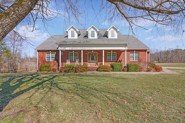 new england style home with covered porch, a shingled roof, a front lawn, and brick siding