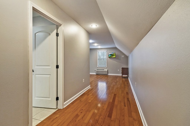 hallway with lofted ceiling, wood-type flooring, an AC wall unit, and baseboards