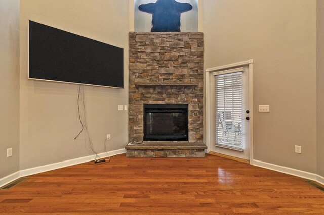 unfurnished living room with visible vents, baseboards, wood finished floors, and a stone fireplace