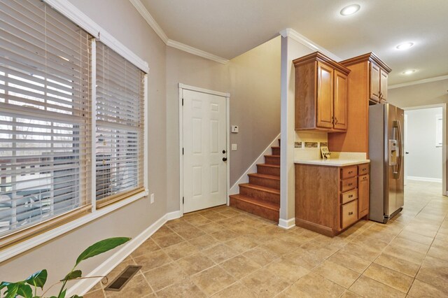 interior space featuring visible vents, light countertops, brown cabinets, stainless steel fridge, and crown molding