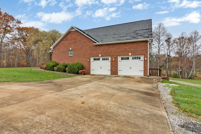 view of side of property with a garage, brick siding, a yard, and roof with shingles