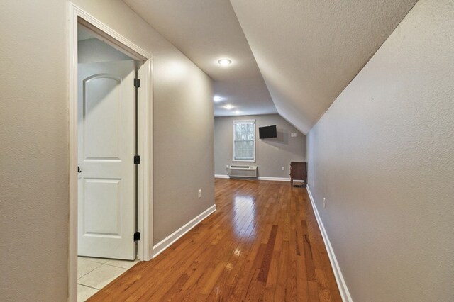 hall with lofted ceiling, a wall unit AC, hardwood / wood-style flooring, and baseboards