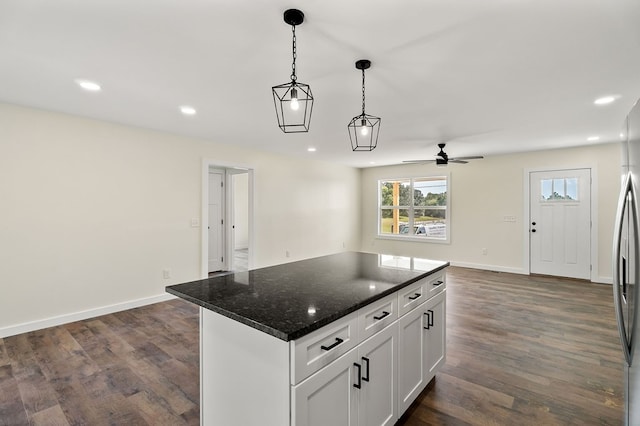 kitchen with a kitchen island, open floor plan, dark stone countertops, hanging light fixtures, and white cabinetry