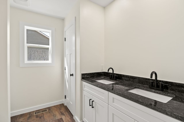 full bath with double vanity, visible vents, a sink, and wood finished floors