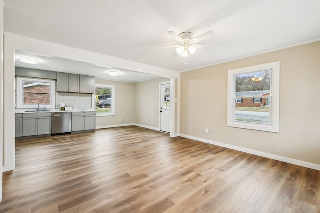 unfurnished living room with crown molding, a ceiling fan, a sink, light wood-type flooring, and baseboards