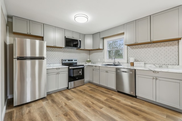 kitchen with light wood finished floors, decorative backsplash, appliances with stainless steel finishes, light stone counters, and a sink