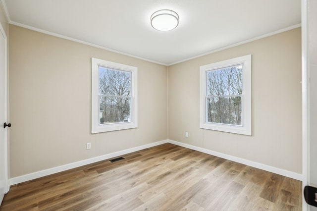 empty room featuring visible vents, ornamental molding, light wood-style flooring, and baseboards