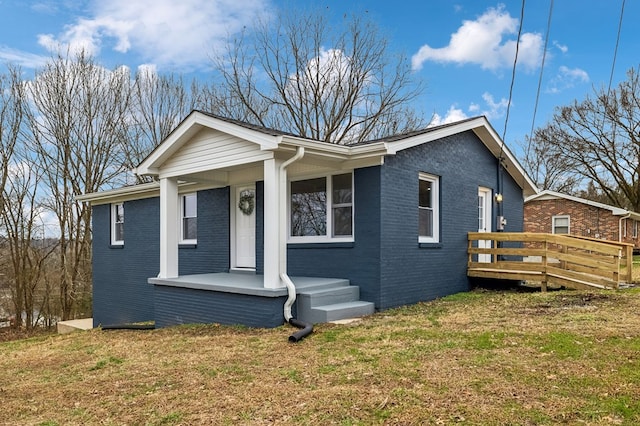 bungalow featuring covered porch, brick siding, a front yard, and a deck