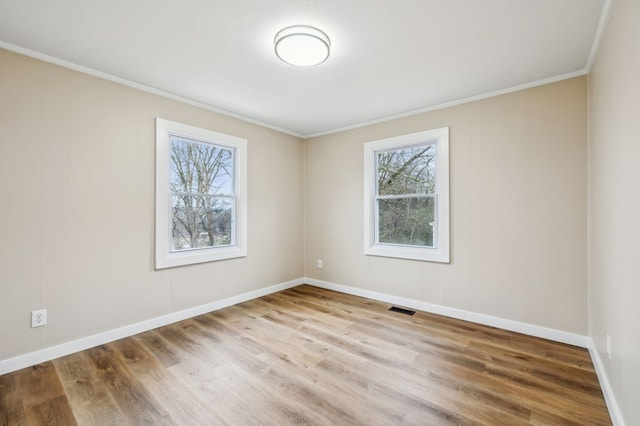 empty room with light wood-style floors, visible vents, crown molding, and baseboards