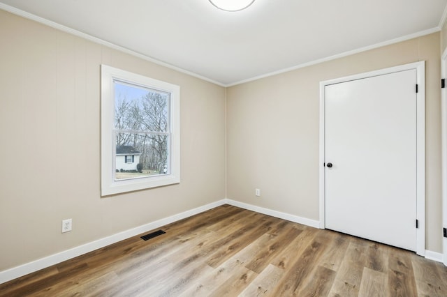 empty room featuring ornamental molding, wood finished floors, visible vents, and baseboards