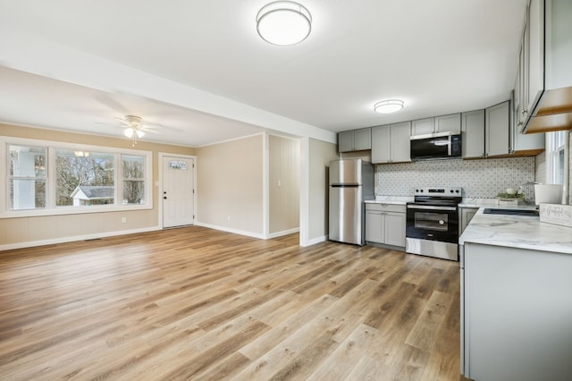 kitchen featuring light wood finished floors, gray cabinets, backsplash, appliances with stainless steel finishes, and light stone countertops