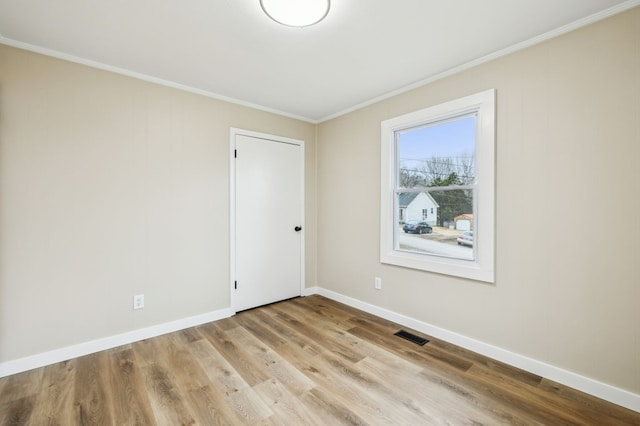 spare room featuring light wood-style floors, visible vents, baseboards, and ornamental molding