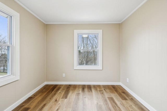 spare room with ornamental molding, light wood-style flooring, a wealth of natural light, and baseboards