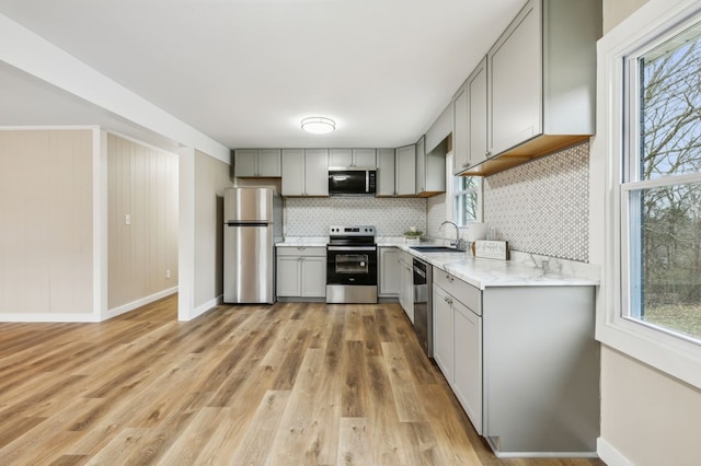 kitchen with tasteful backsplash, appliances with stainless steel finishes, gray cabinetry, light wood-style floors, and a sink