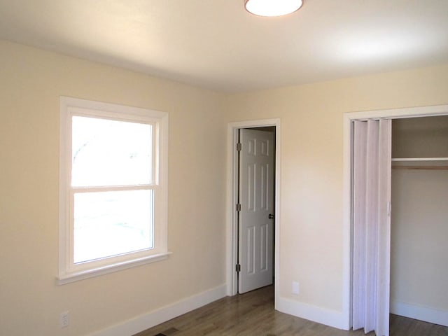 unfurnished bedroom featuring wood finished floors, baseboards, and a closet