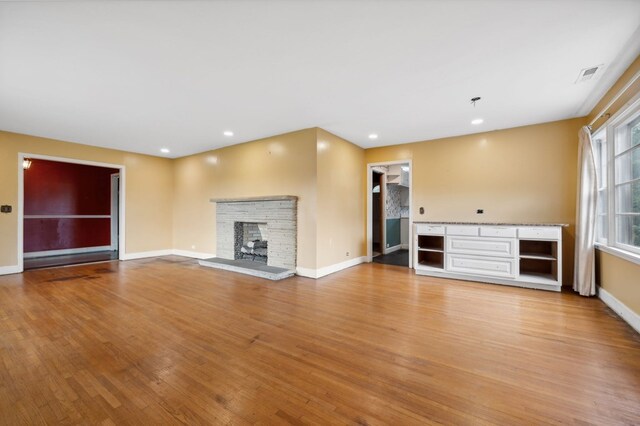 unfurnished living room with a stone fireplace, recessed lighting, visible vents, baseboards, and light wood-style floors