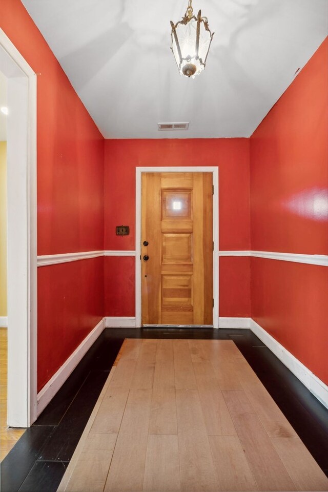 doorway to outside with a chandelier, visible vents, baseboards, and wood finished floors