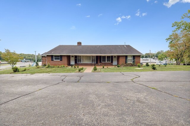 ranch-style home with a front yard, covered porch, brick siding, and a chimney