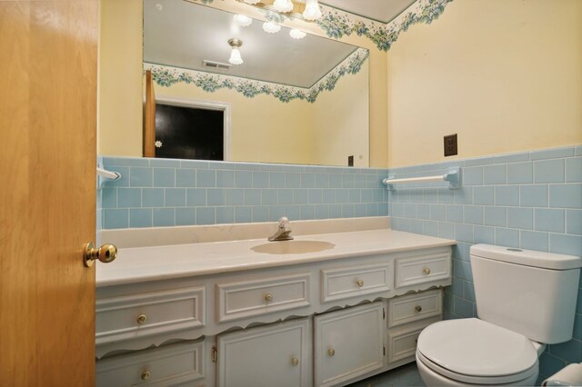 bathroom with toilet, a wainscoted wall, visible vents, vanity, and tile walls